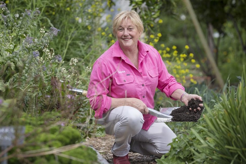 A woman in gardening clothes crouched in a garden holding soil.