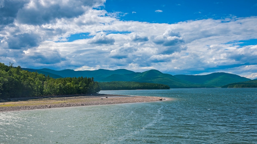 A glittering reservoir lake is seen on a bright, windy day, with undulating green mountains in the distance.