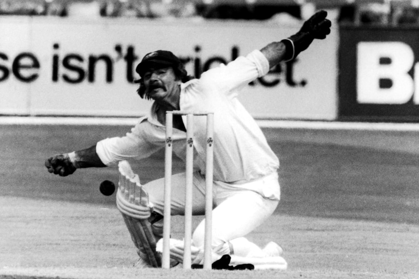 Rod Marsh stretches his arms out behind the stumps