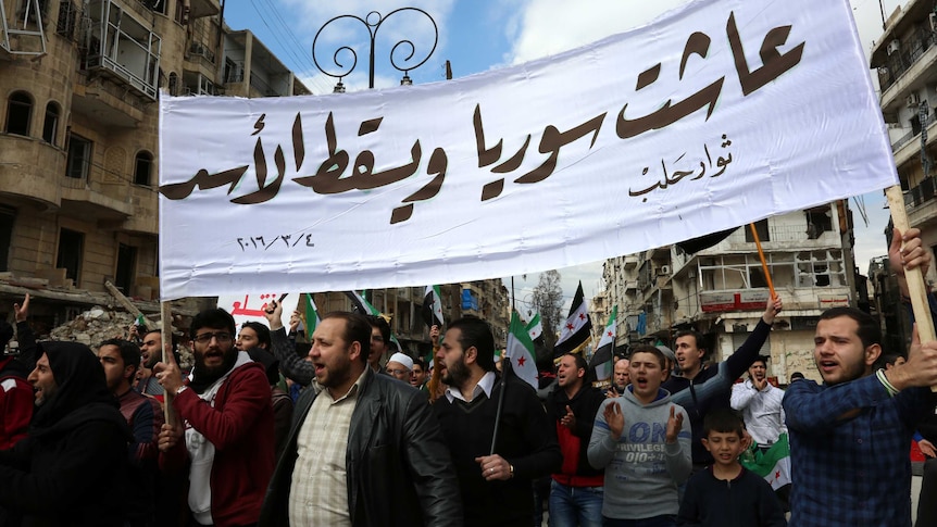 Syrian civilians and activists hold a banner reading in Arabic "Long live Syria, down with Assad"