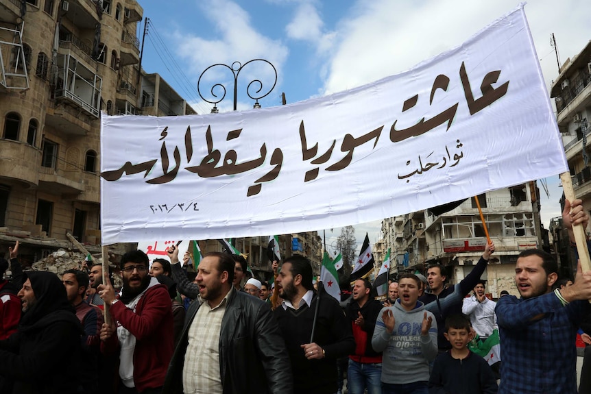 Syrian civilians and activists hold a banner reading in Arabic "Long live Syria, down with Assad"