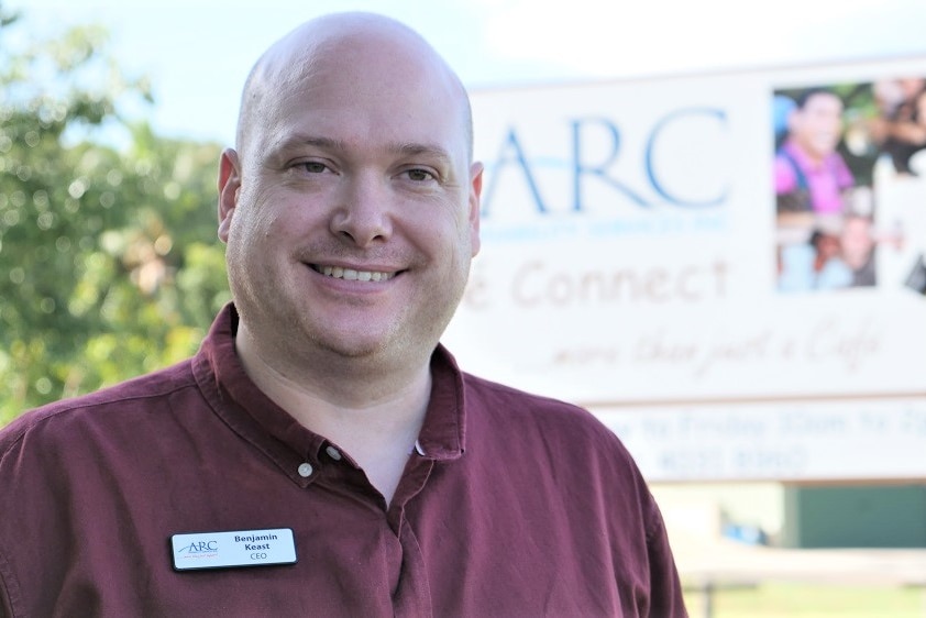 Young man in maroon-coloured shirt standing in front of ARC Disability Services sign outside