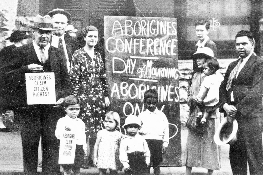 A black and white photo of a group of people standing by a sign calling for Aboriginal rights.