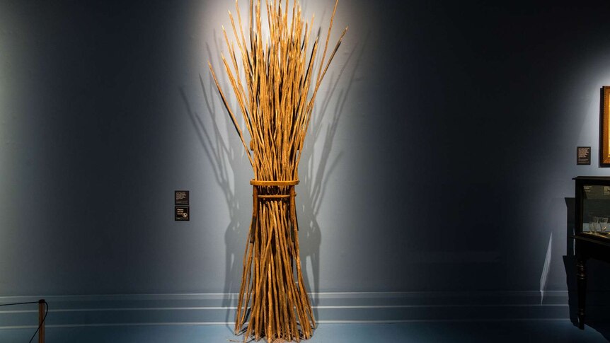 3-metre-high sculpture mounted on wall, made from wooden chair with seat torn out and hole holding bundle of tea-tree sticks.