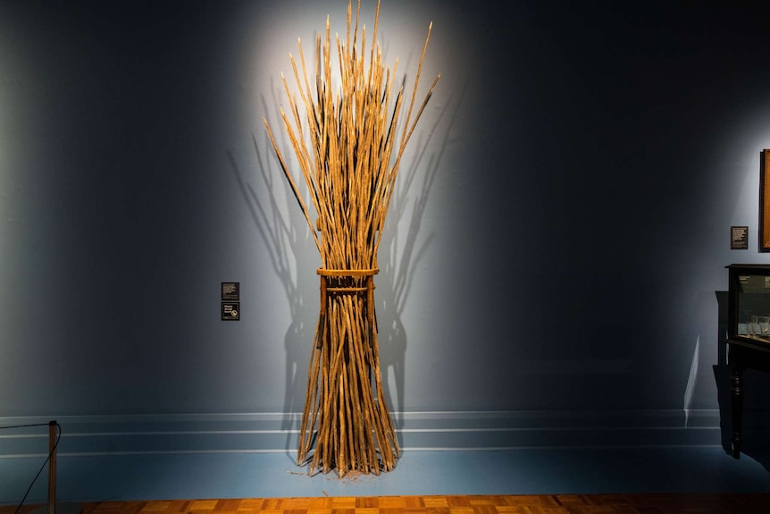 3-metre-high sculpture mounted on wall, made from wooden chair with seat torn out and hole holding bundle of tea-tree sticks.