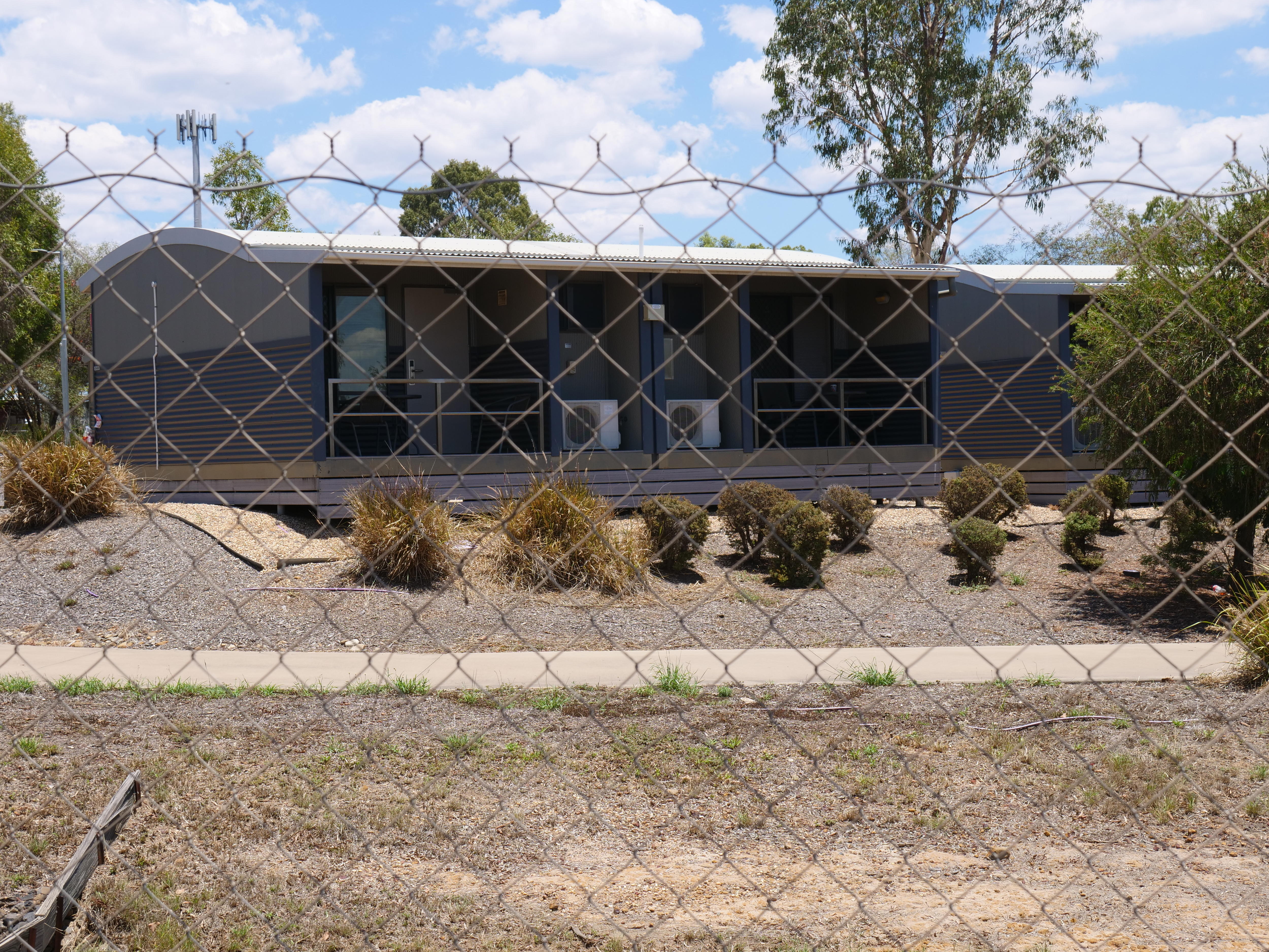 Una casa grande con techo redondo y arbustos en la parte delantera. La foto fue tomada a través de una alambrada.