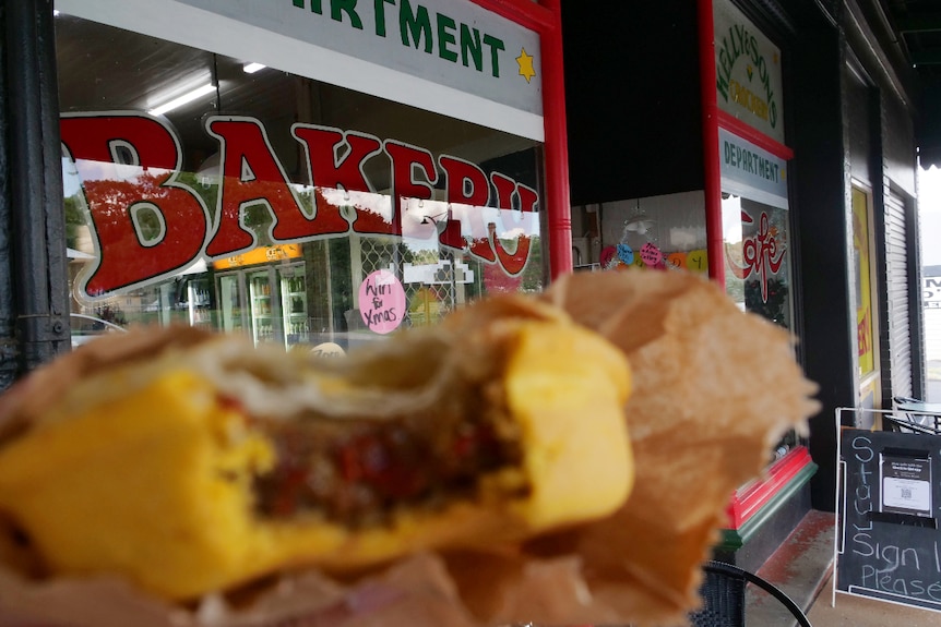 Meat pie with a bite out of it with a bakery sign in focus