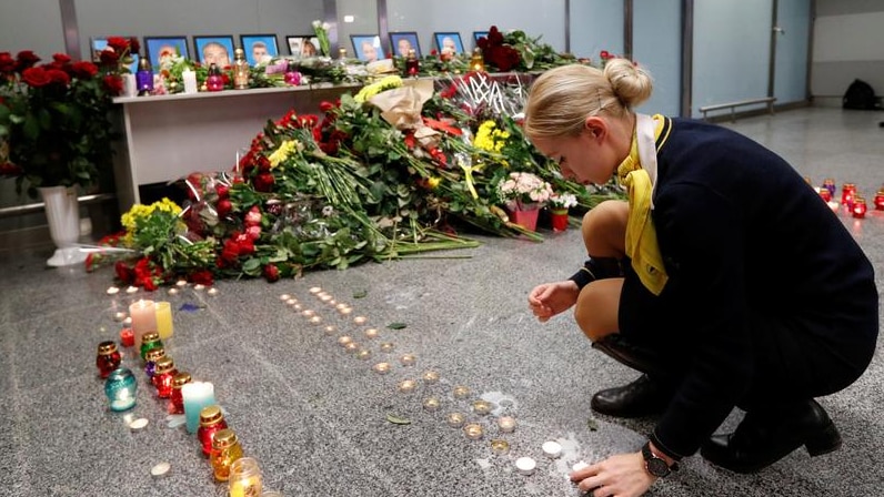 A woman lights a candle at a memorial.