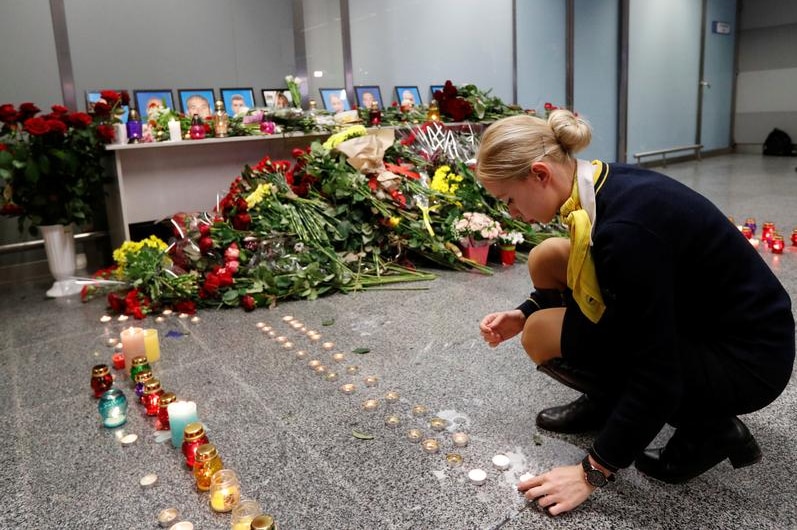 A woman lights a candle at a memorial.