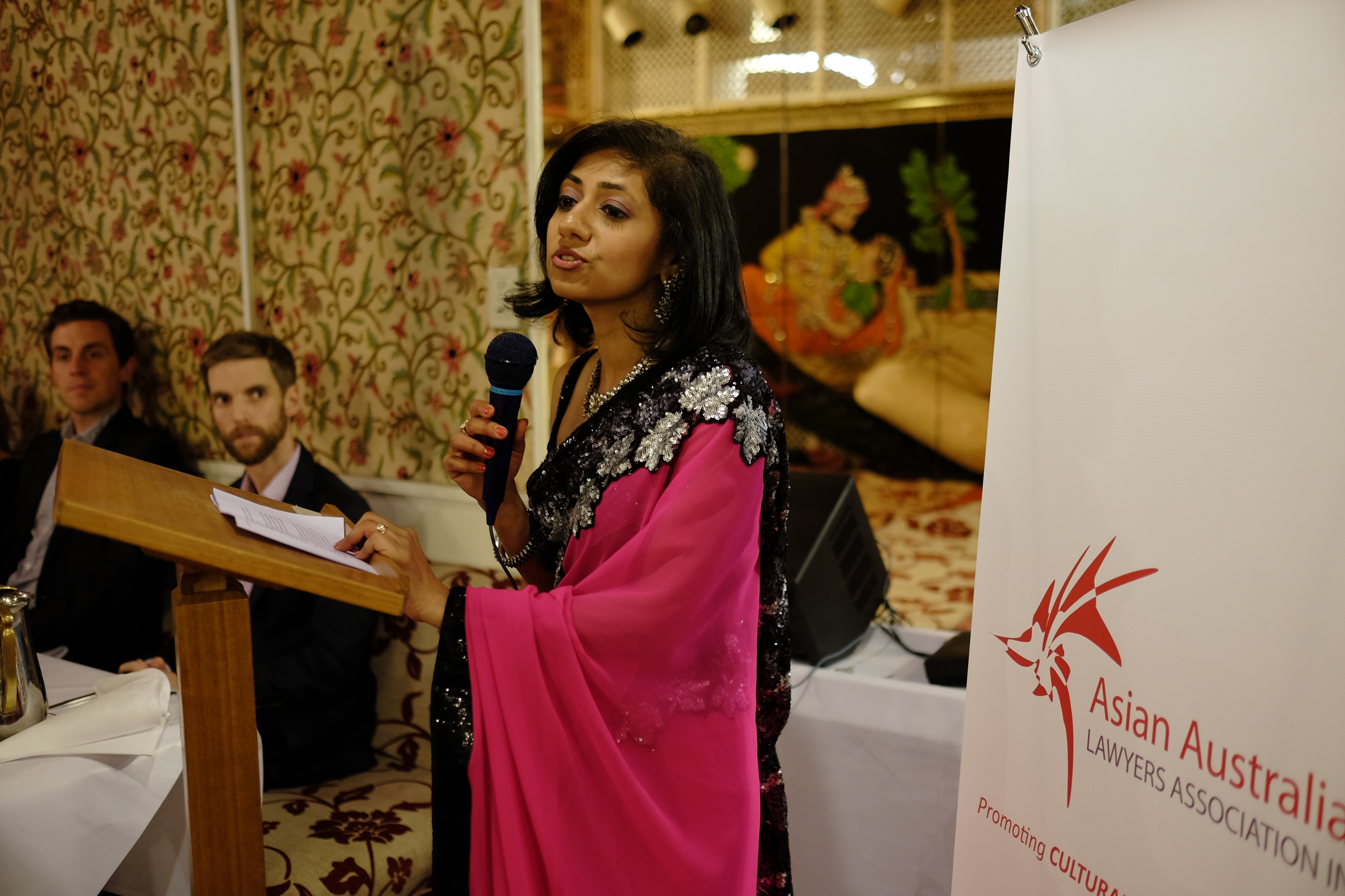 Molina addresses a crowd while wearing a bright pink sari with black and silver beading. 
