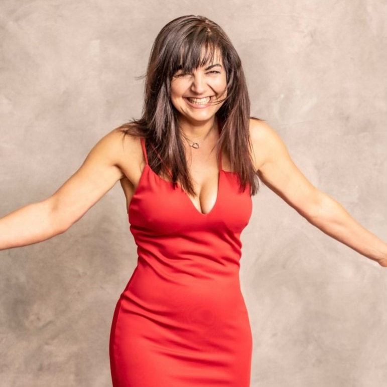 A woman in a red dress smiles with her arms outstretched.