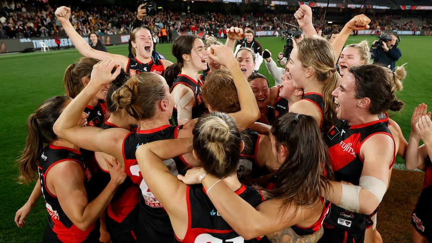 Essendon celebrate as a team, after beating Hawthorn at Docklands Stadium in their AFLW season seven opener.