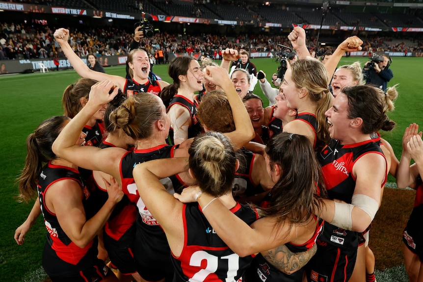 Essendon celebrate as a team, after beating Hawthorn at Docklands Stadium in their AFLW season seven opener.