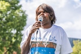 A woman speaks into a microphone. Her t-shirt reads 'water is life'.
