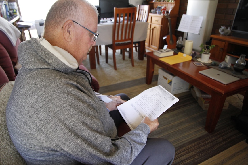 A man sitting on a chair in his lounge room reads a document.