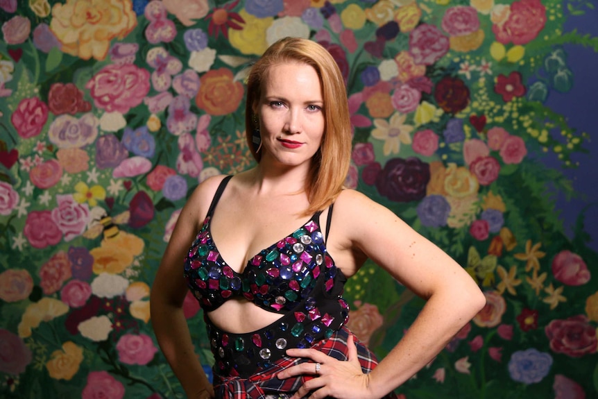 Colour photography of Bey Dance director Liz Cahalan posing in dance outfit in front of painted floral wallpaper wall.