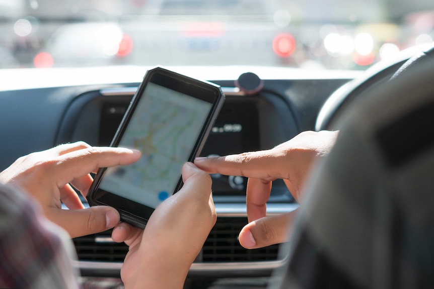 A couple in a car are pointing at their smartphone showing a mapping app