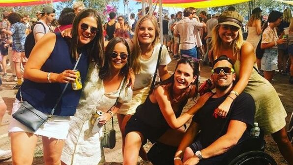 Dylan Alcott and five friends celebrating at a music festival under an orange and yellow tent