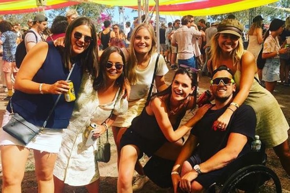 Dylan Alcott and five friends celebrating at a music festival under an orange and yellow tent