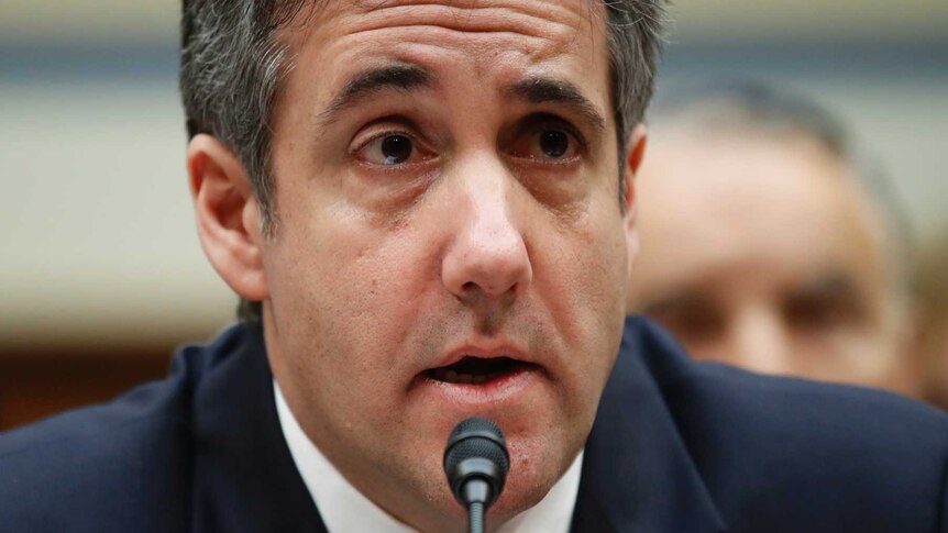 Michael Cohen wearing a blue tie speaking into a microphone.