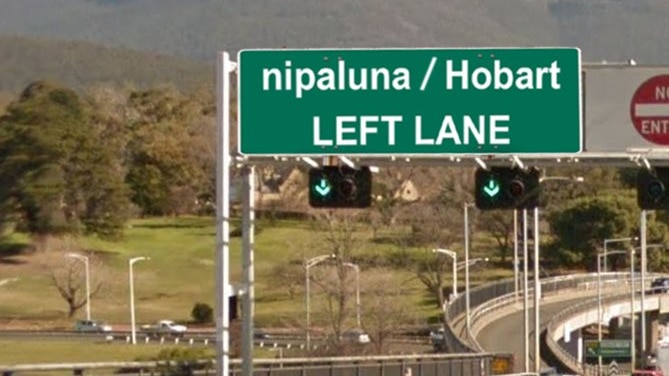 Cars drive along a Tasmanian highway under a sign using both English and traditional names for the capital, Hobart and nipaluna