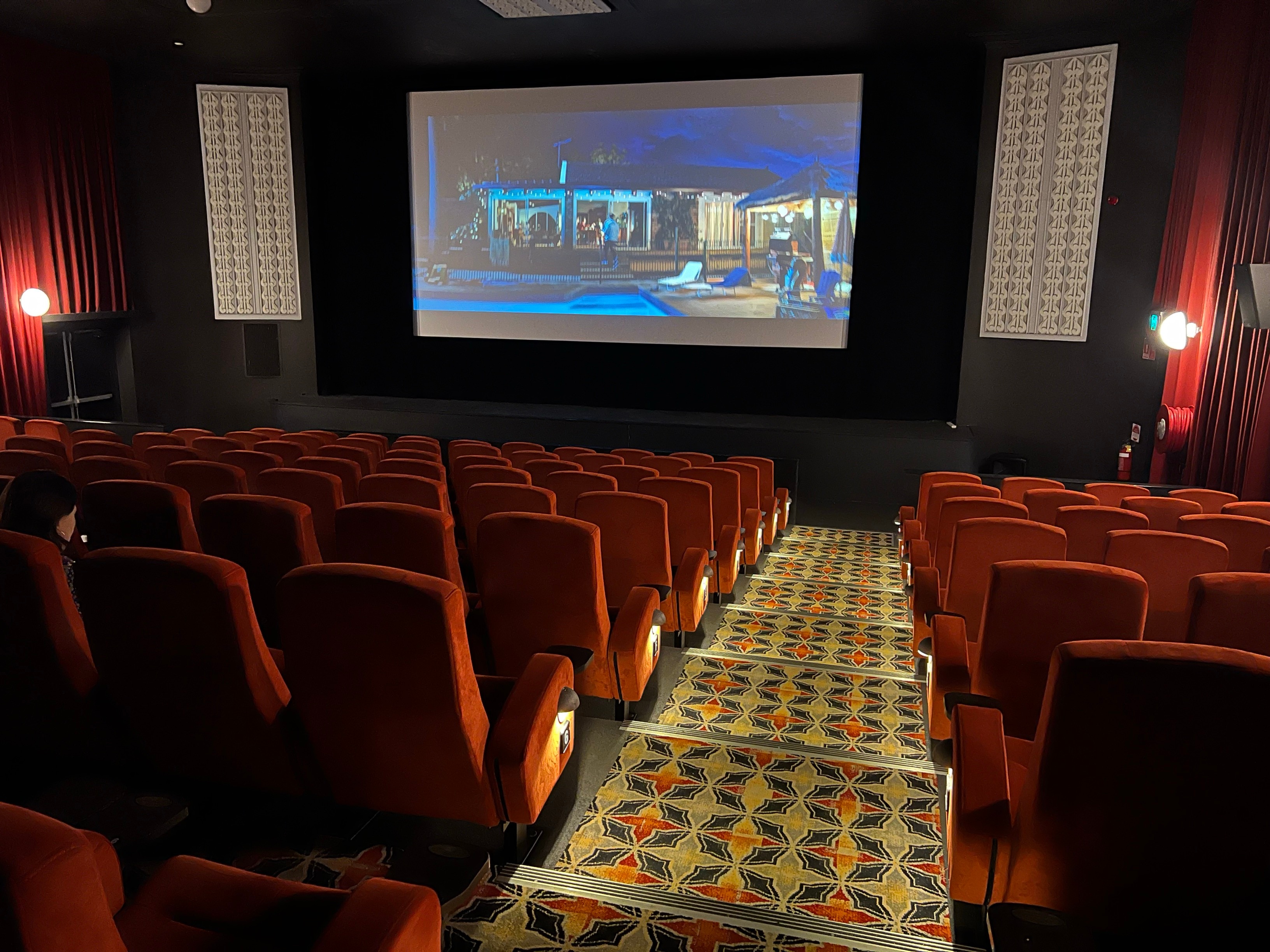 The inside of a movie theatre with red velvet seats, a yellow, orange, blue pattern carpet going down the steps.