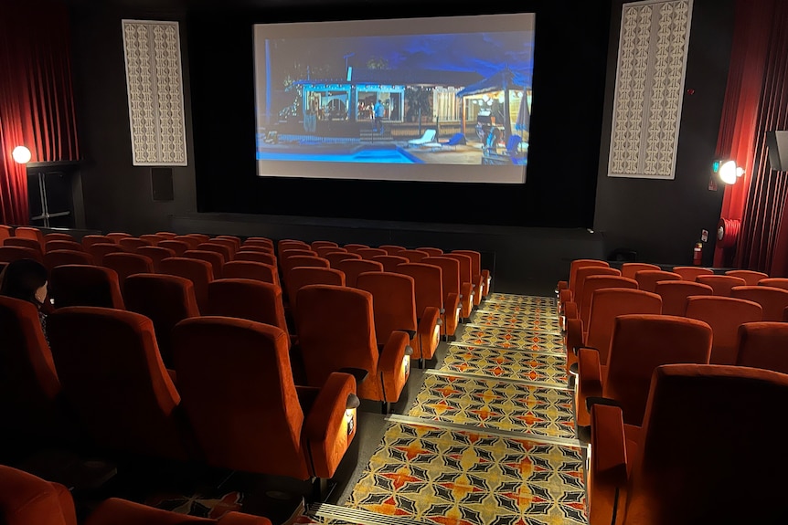 The inside of a movie theatre with red velvet seats, a yellow, orange, blue pattern carpet going down the steps.