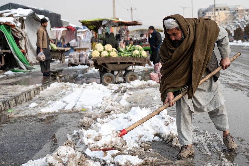 An Afghan vegetable vendor shovels snow along a street in Kabul.