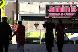 people walking in the street under a restaurant sign