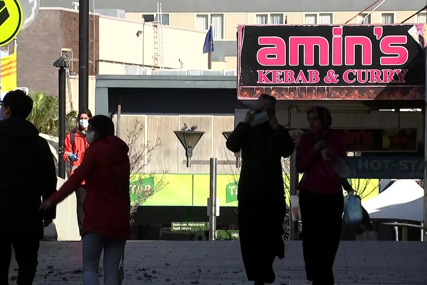 people walking in the street under a restaurant sign