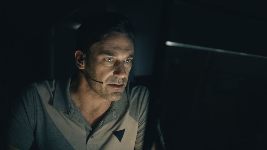 Jon Hamm sits in a dark room in front of a computer with a headset