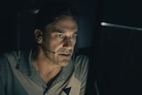 Jon Hamm sits in a dark room in front of a computer with a headset