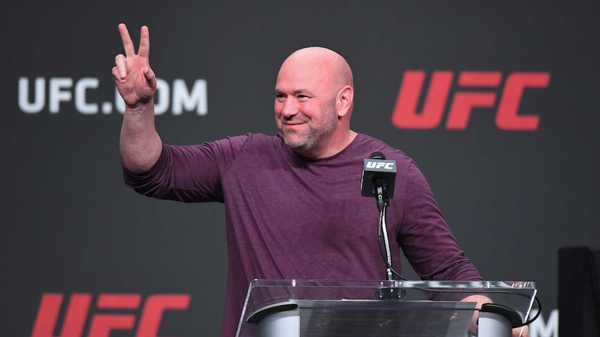 Dana White stands and looks off to one side, holding one hand up with two fingers stretched out