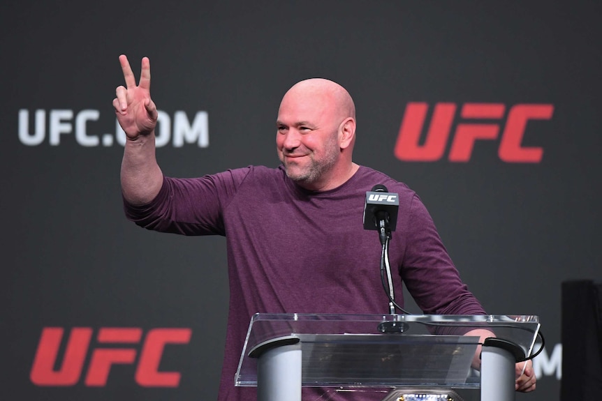 Dana White stands and looks off to one side, holding one hand up with two fingers stretched out