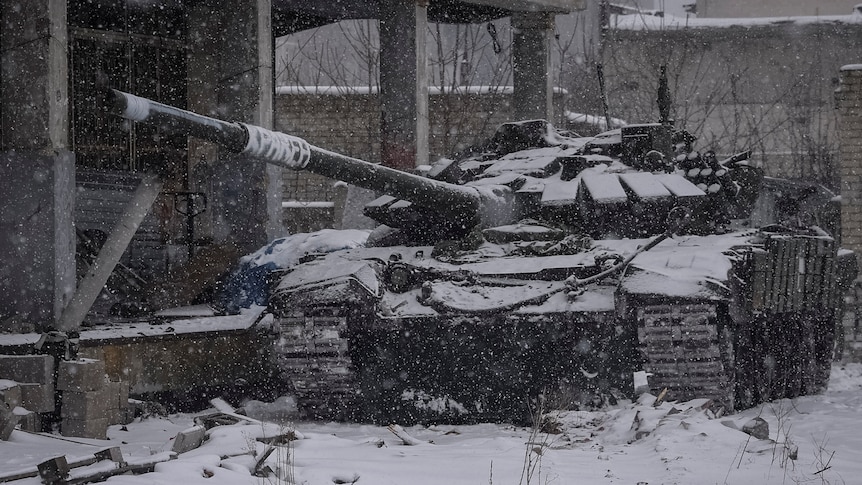 A Ukrainian tank is parked near a building as snow falls. 