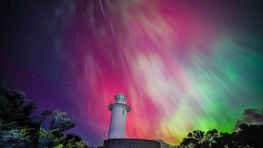 A lighthouse photographed in front of a pink, blue, green and yellow sky