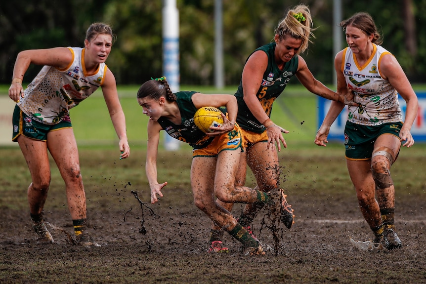 a woman with a football running through mud with three other players in the background. 