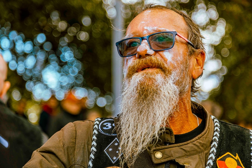 Tony Russell is a man with a large beard, wearing a black vest with the Aboriginal flag on it.