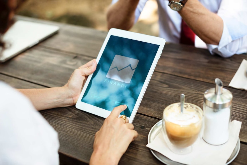 Lady holding an iPad talking to her husband over coffee.