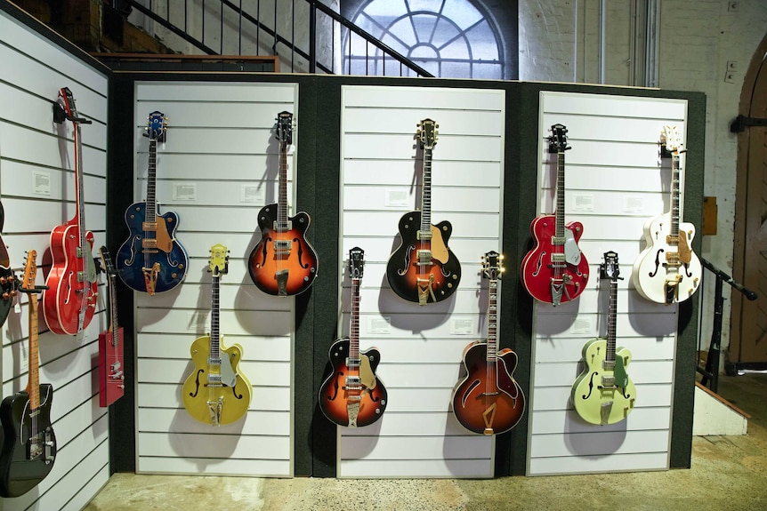 An array of colourful guitars are on display on the wall of an exhibit space.