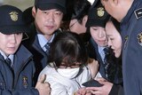 Choi Soon-sil, escorted by security officers and wearing a white jumpsuit and surgical mask, arrives for questioning.