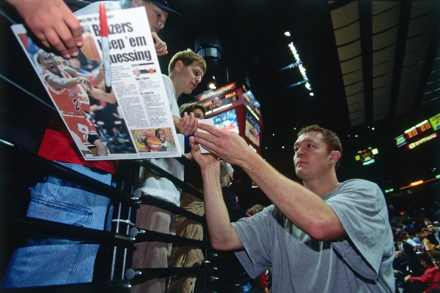 Fans lean over to give items to bulls player luc longley to sign