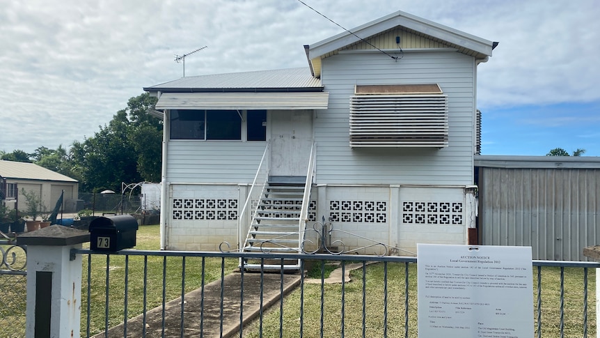 small blue Queenslander home with rates sign in front