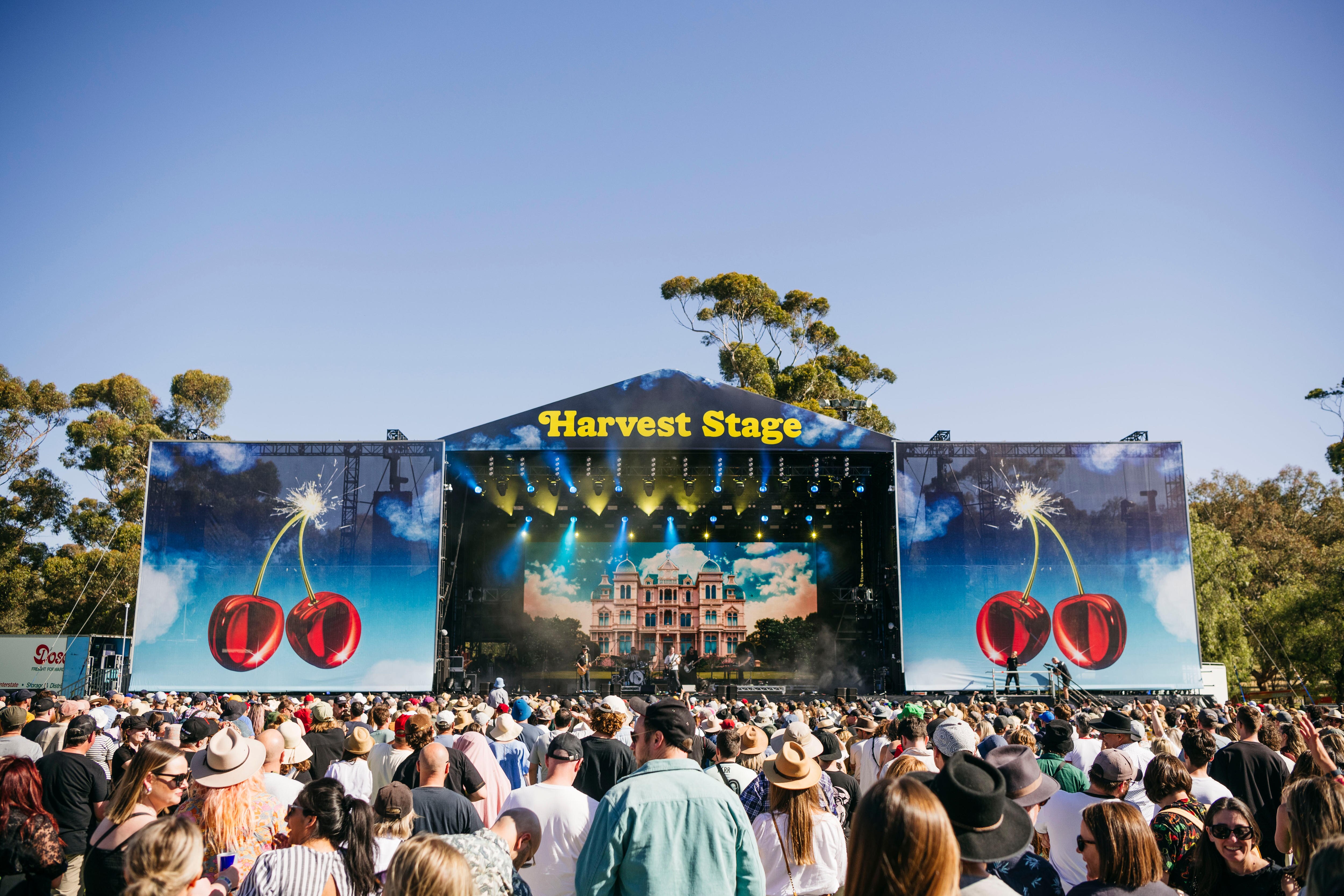 A crowd of people in front of a big festival stage on a clear day