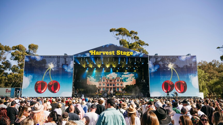 A crowd of people in front of a big festival stage on a clear day