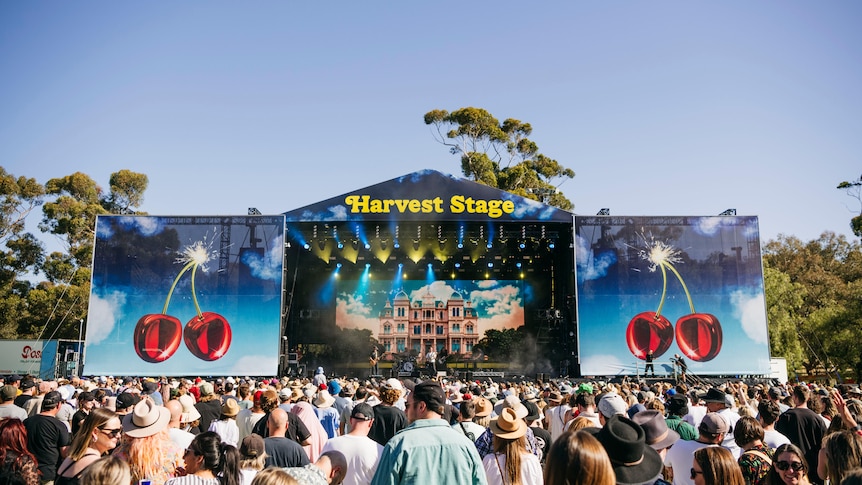 A crowd of people in front of a big festival stage on a clear day