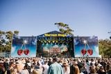 A crowd of people in front of a big festival stage on a clear day