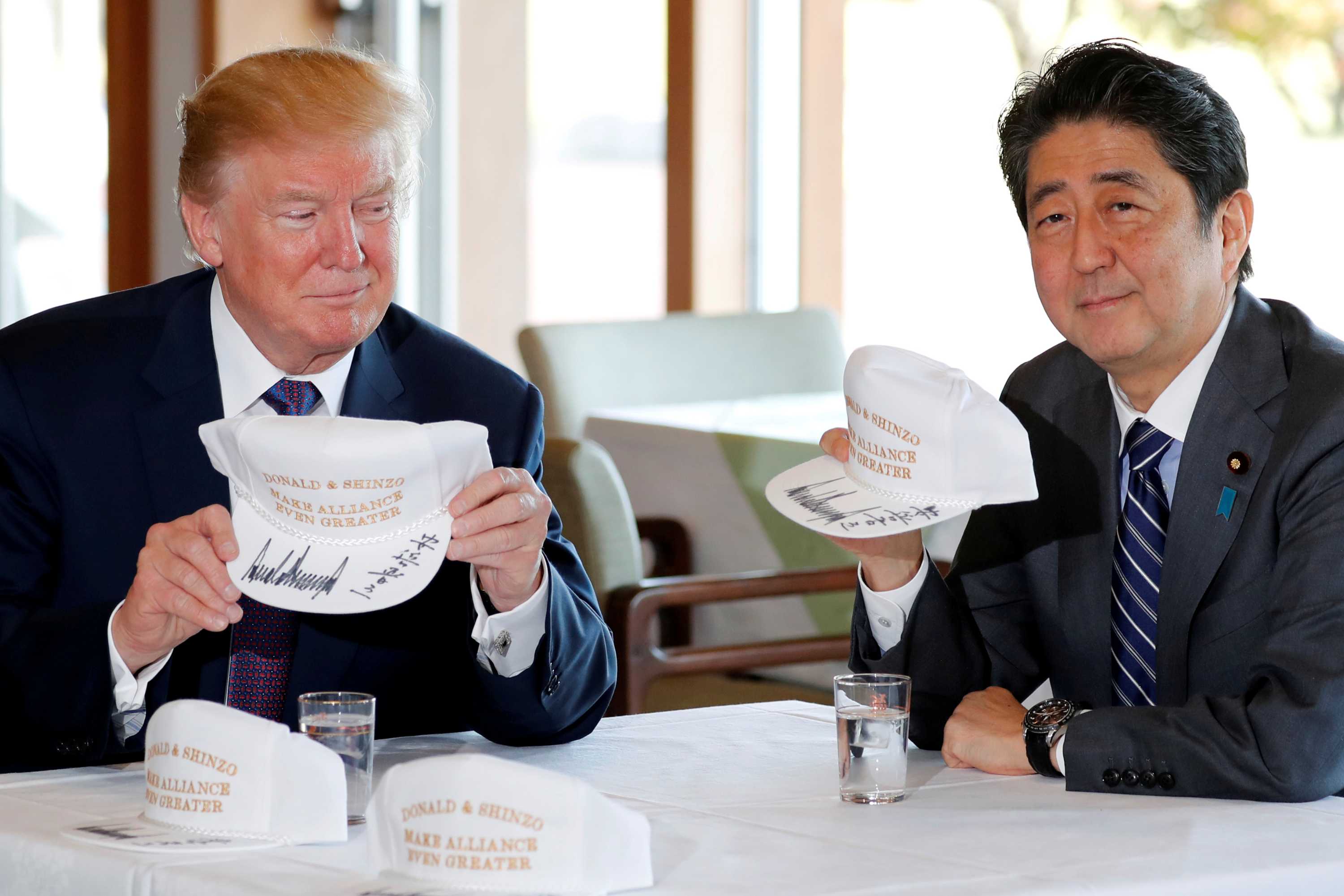 Donald Trump and Shinzo Abe hold hats they signed reading 'Donald & Shinzo Make Alliance Even Greater'.