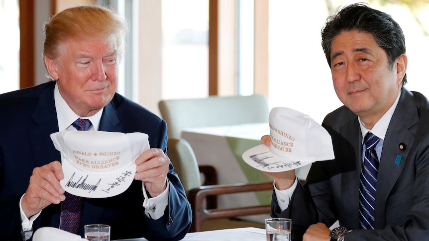 Donald Trump and Shinzo Abe hold hats they signed reading 'Donald & Shinzo Make Alliance Even Greater'.