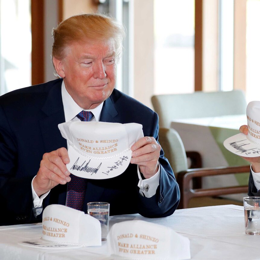 Donald Trump and Shinzo Abe hold hats they signed reading 'Donald & Shinzo Make Alliance Even Greater'.